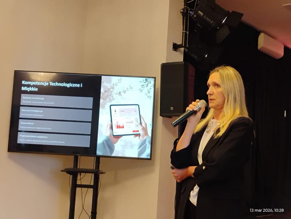 Kobieta prowadząca prezentację. Obok niej ekran wyświetla slajd dotyczący kompetencji technologicznych i miękkich, z listą zagadnień oraz grafiką tabletu.