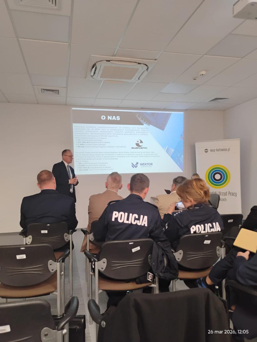 Grupa osób uczestnicząca w spotkaniu informacyjnym, patrząca na slajd przedstawiający informacje o firmie WEKTOR Consulting oraz Systemo.